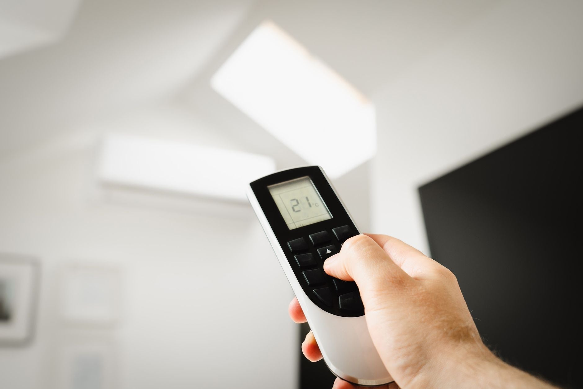 Close-up of a hand holding a remote control to adjust indoor climate settings