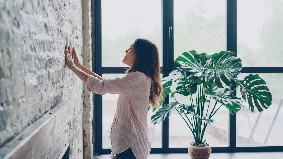Woman adjusting a smart thermostat on the wall of a bright modern home