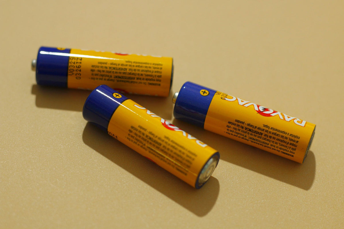 Three AA alkaline batteries on a beige surface