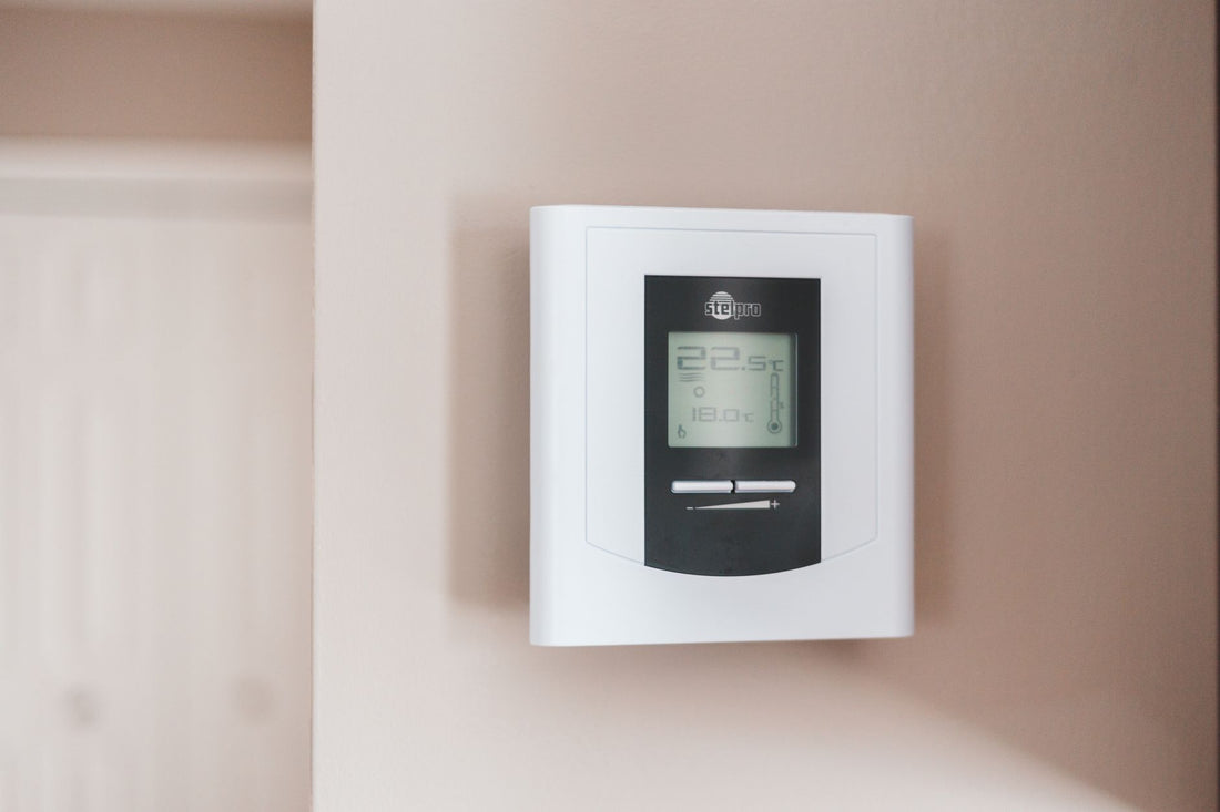 White digital programmable thermostat mounted on a wall displaying the current temperature